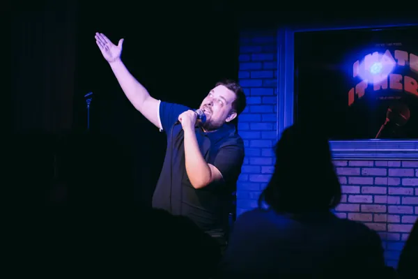Dan onstage holding a microphone and raising one arm toward the lights.