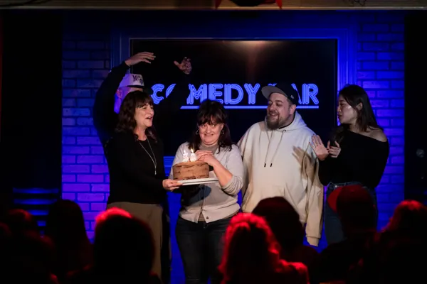 A group on the Comedy Bar stage celebrating with a birthday cake.